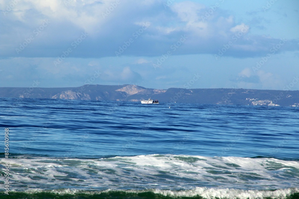 Fototapeta premium Small sailing boat is pictured in the open ocean, with a stunning mountainous landscape