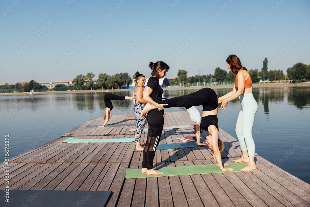 A pair yoga class with an instructor on a wooden pier on the river in the city. A group of women train outdoors in the morning.