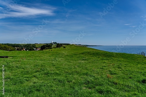 grassy hill with a lone bench near water, under a bright blue sky photo
