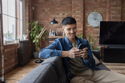 Happy mid adult male using smartphone sitting on a sofa in his loft apartment