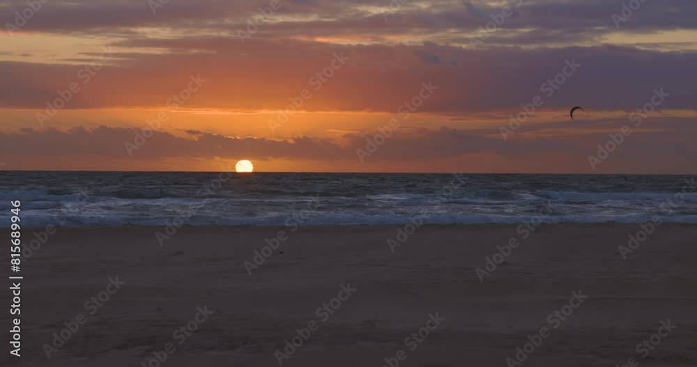 Kitesurfers on board with kite surfing in the ocean with calm waves at sunset next to beach Kitesurfers on board with kite surfing in the ocean with calm waves at sunset next to beach