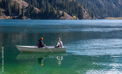 A view of lake and the beautiful mountain range in the background. Lovers ride in a boat on a lake. Happy couple woman and man together relaxing on the water. The beautiful nature around.