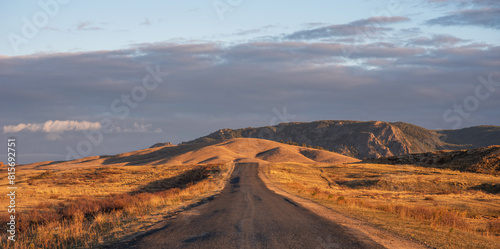 Sunrise on an empty country road passing through amazing hilly landscape. Colorful grassy and hilly natural landscape in autumn. Beautiful autumn scenery in Inner Mongolia  China.