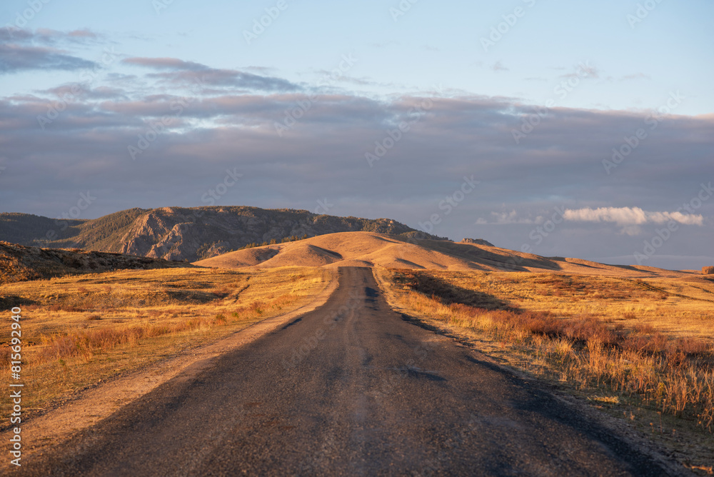 Sunrise on an empty country road passing through amazing hilly landscape. Colorful grassy and hilly natural landscape in autumn. Beautiful autumn scenery in Inner Mongolia, China.