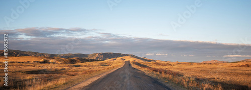 Straight country road through the autumn landscape in a hilly area. Grassy field and hills. Rural landscapes.