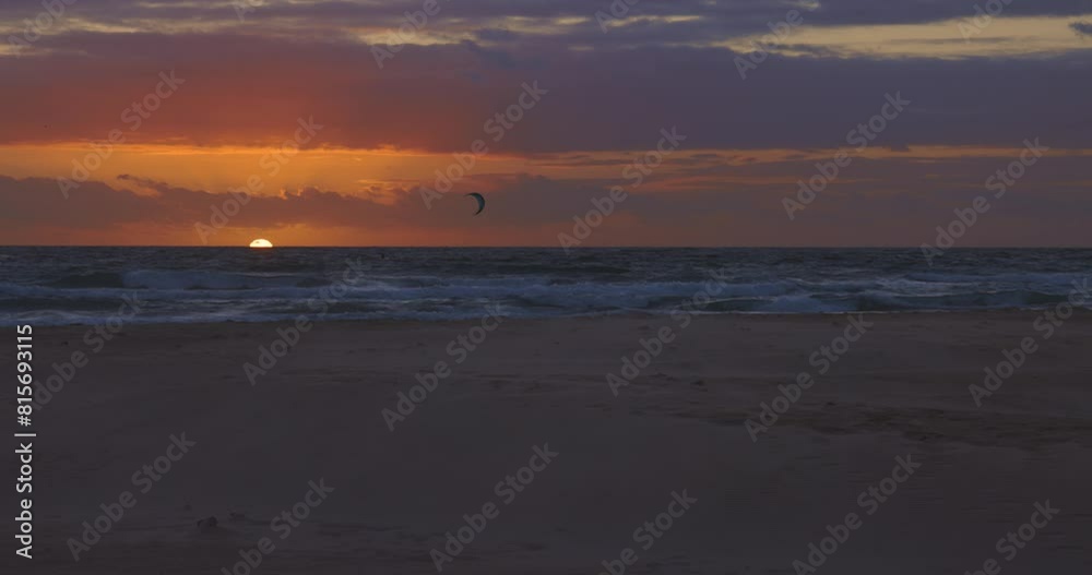 Kitesurfer kiting with kite and board in the ocean with calm waves at sunset with sun in the background Kitesurfer kiting with kite and board in the ocean with calm waves at sunset with sun in the background