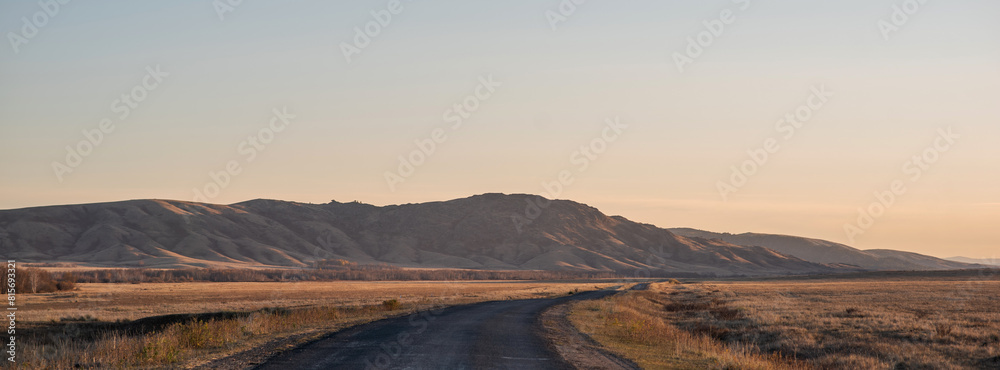 Fototapeta premium Sunrise on an empty country road passing through amazing hilly landscape. Colorful grassy and hilly natural landscape in autumn. Beautiful autumn scenery in Inner Mongolia, China.