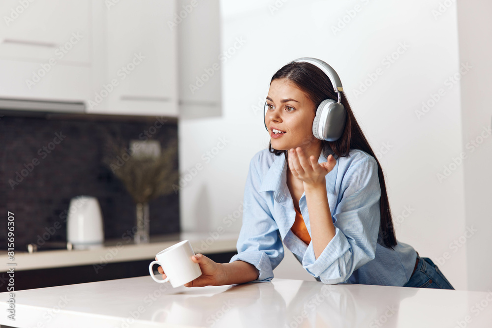 Woman enjoying music with headphones while sitting at table in modern kitchen, lifestyle concept Woman enjoying music with headphones while sitting at table in modern kitchen, lifestyle concept