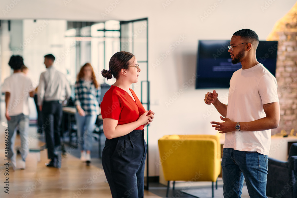 Obraz premium Young business colleagues, including an African American businessman, engage in a conversation about business issues in the hallway of a modern startup coworking center, exemplifying dynamic problem