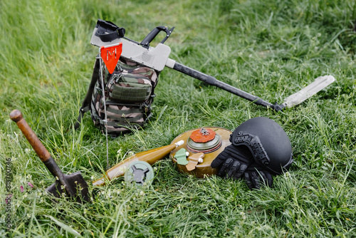 Explosive devices and a metal detector lie on the background of a forest massif. Equipment for demining the territory