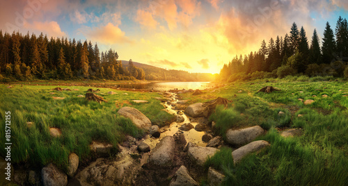 Spectacular sunrise over a scenic landscape with colorful clouds, trees, grasslands and water reflecting the golden sunlight