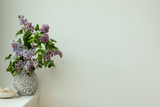 Simple compositions of lilac flowers bouquet in design vase,  white wall, template copy space.