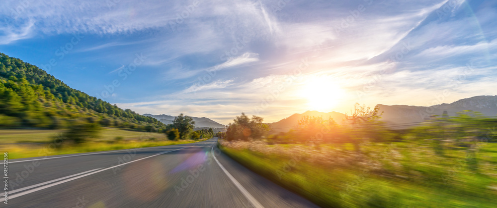 Mediterranean sea coast road into mountains horizon in summer with beautiful bright sun rays - wide angle panorama shot with high speed motion blur effect