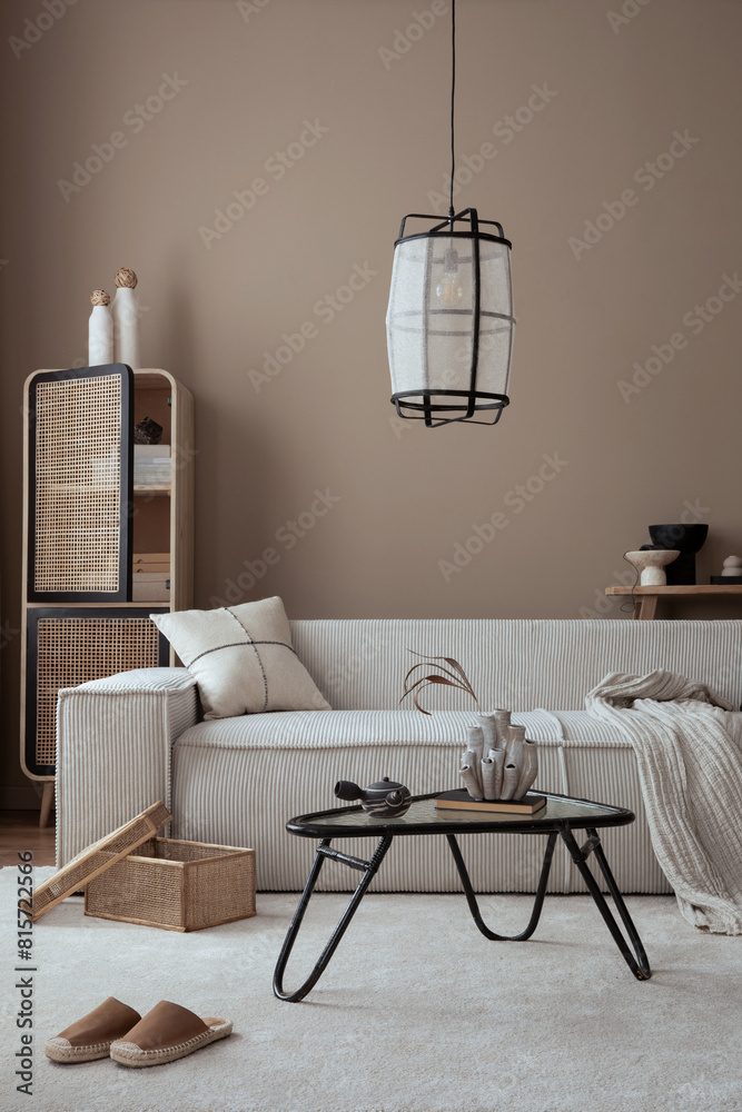 Obraz premium Warm and cozy living room interior with modular sofa, beige wall, carpet, glass coffee table, rattan sideboard, slippers, wooden bench, stylish lamp and personal accessories. Home decor. Template.