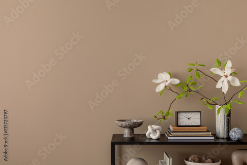 Minimalist composition of living room interior with copy space, black rack, brown wall, clock, vase with magnolia, marble bowl, books and personal accessories. Home decor. Template.