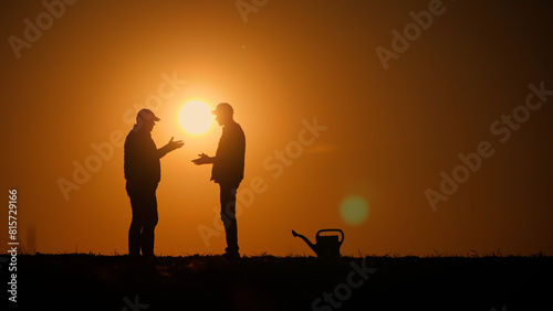 Two male farmers communicate in a field at sunset  shaking hands
