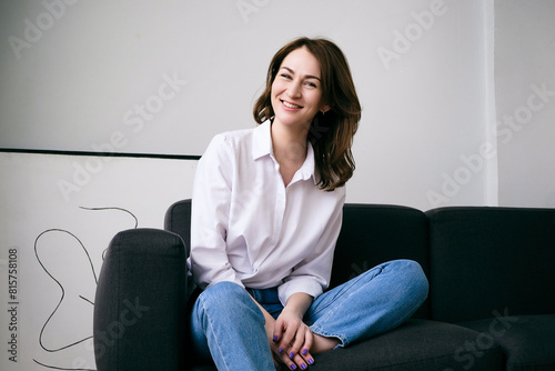 young smiling woman in blue jeans and a white shirt is sitting on the sofa