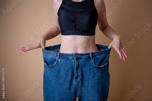 Slim young woman in big jeans showing successful weight loss with her thumb up photo