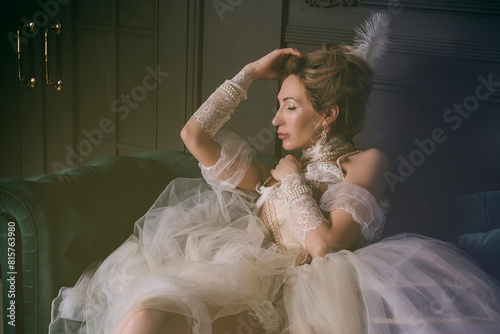 a young woman in an 18th century dress and lace in a boudoir is sitting in an armchair in a sexy and sensual way photo