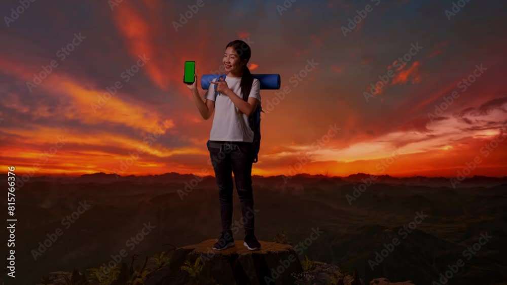 Full Body Of Asian Female Hiker With Mountaineering Backpack Smiling And Pointing To Mock Up Green Screen Smartphone While Standing On The Top Of Mountain During Sunset Time Full Body Of Asian Female Hiker With Mountaineering Backpack Smiling And Pointing To Mock Up Green Screen Smartphone While Standing On The Top Of Mountain During Sunset Time