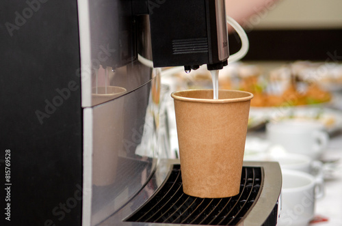 Coffee machine makes coffee with milk in a paper brown cup at a public event, banquet, without people
