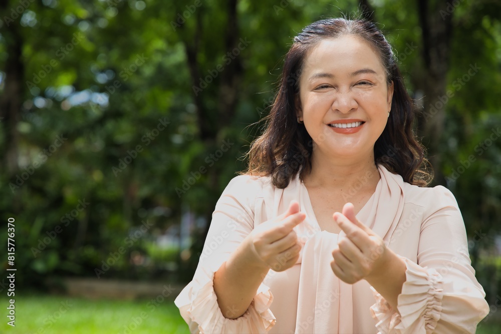 Happy Smiling Middle Aged Asian woman showing heart hand gesture with positive expression and emotion, concept image for love, care, friendship Happy Smiling Middle Aged Asian woman showing heart hand gesture with positive expression and emotion, concept image for love, care, friendship