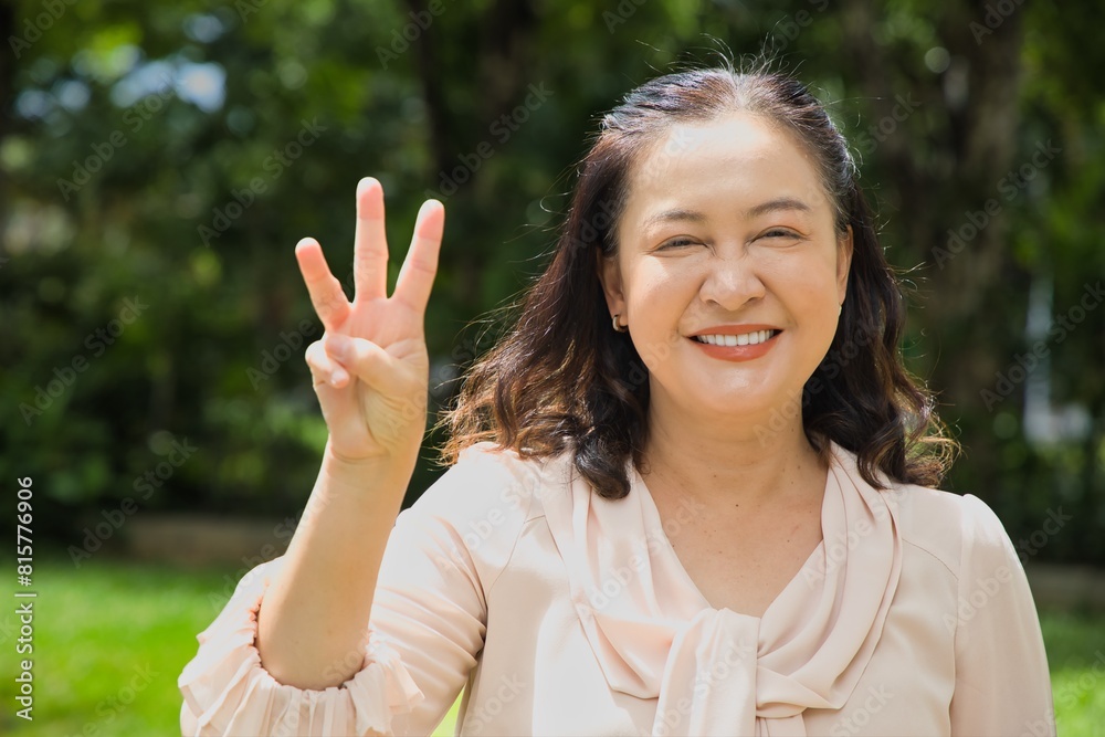 Healthy happy smiling middle aged asian woman pointing 3 fingers up, concept of three points, number three, third count in summer green park Healthy happy smiling middle aged asian woman pointing 3 fingers up, concept of three points, number three, third count in summer green park