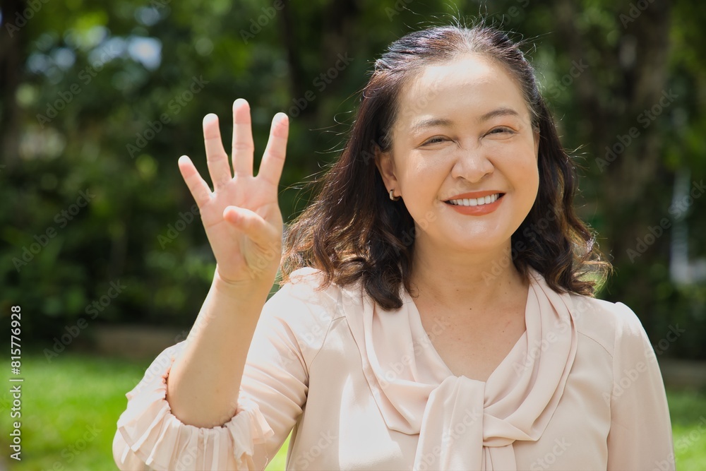 Healthy happy smiling middle aged asian woman pointing 4 fingers up, concept of four points, number four, forth count in summer green park Healthy happy smiling middle aged asian woman pointing 4 fingers up, concept of four points, number four, forth count in summer green park