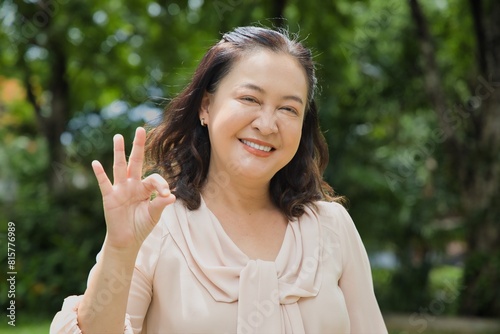 Middle aged woman showing yes, approving, accepting ok for all correct hand gesture in summer green outdoor park