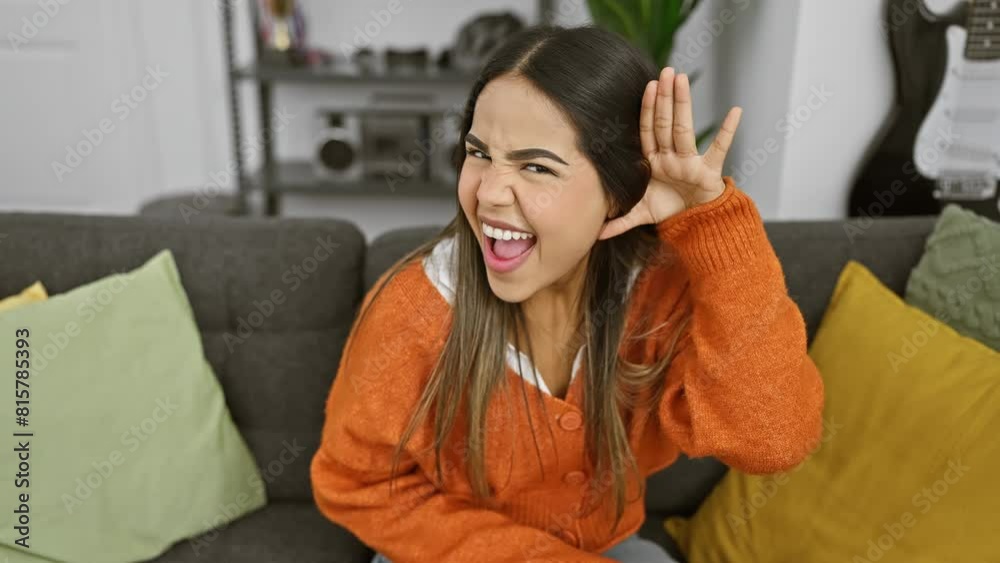 Beautiful young latin woman in sweater, sits on sofa at home, eagerly listening to thrilling gossip, hand to ear. a deafness issue? Beautiful young latin woman in sweater, sits on sofa at home, eagerly listening to thrilling gossip, hand to ear. a deafness issue?