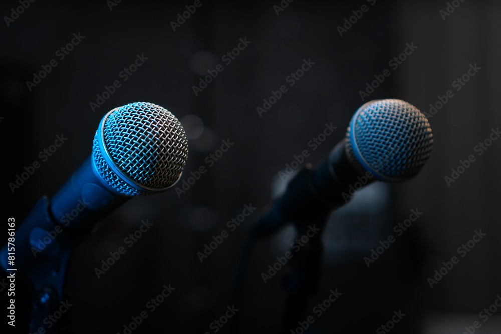 Close-up of two microphones with blue backlight in a music studio, at a concert in the dark, copy space. Selective focus Close-up of two microphones with blue backlight in a music studio, at a concert in the dark, copy space. Selective focus