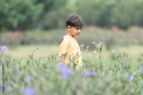 Happy little 4 year old Caucasian boy standing in flowers field smiling, sunny day. Cute child boy playing outdoors in summer in nature