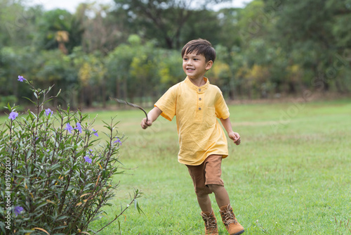 Happy little 4 year old Caucasian boy running in field with flowers garden smiling, laughing, sunny day. Cute child boy playing outdoors in summer in nature