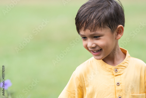 Happy little 4 year old Caucasian boy looking at flower, smiling, laughing, sunny day. Cute child boy playing outdoors in summer in nature. Green background