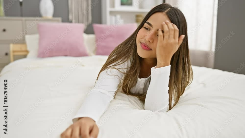 A young, smiling hispanic woman lounging in a tidy bedroom with white beddings and pink pillows, evoking a sense of relaxation and comfort. A young, smiling hispanic woman lounging in a tidy bedroom with white beddings and pink pillows, evoking a sense of relaxation and comfort.