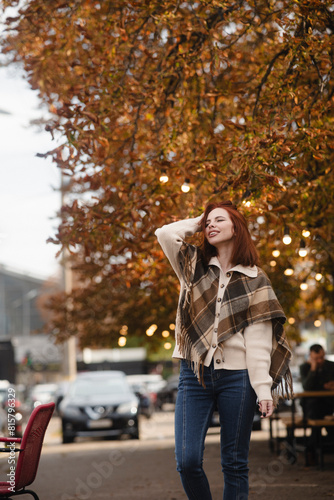 A merry red-haired girl radiates happiness as she walks through the autumn city streets.