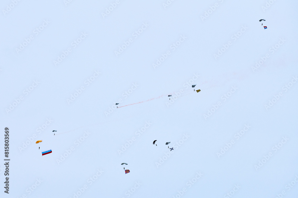 Obraz premium Airborne forces paratroopers soaring holding Flag of Russia and flags of military units, military exercise for celebration of Airborne Forces Day with formation landing, army airborne division descend