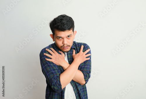 Portrait of asian guy shivering, trembling and feeling cold, hugging himself to warm up, shaking and chattering teeth during frosty weather, isolated over studio background, banner, panorama. © IgnatiusHarly