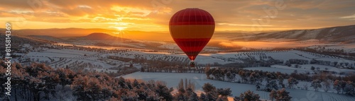 Hot air balloon flies over snow-covered landscape at sunrise