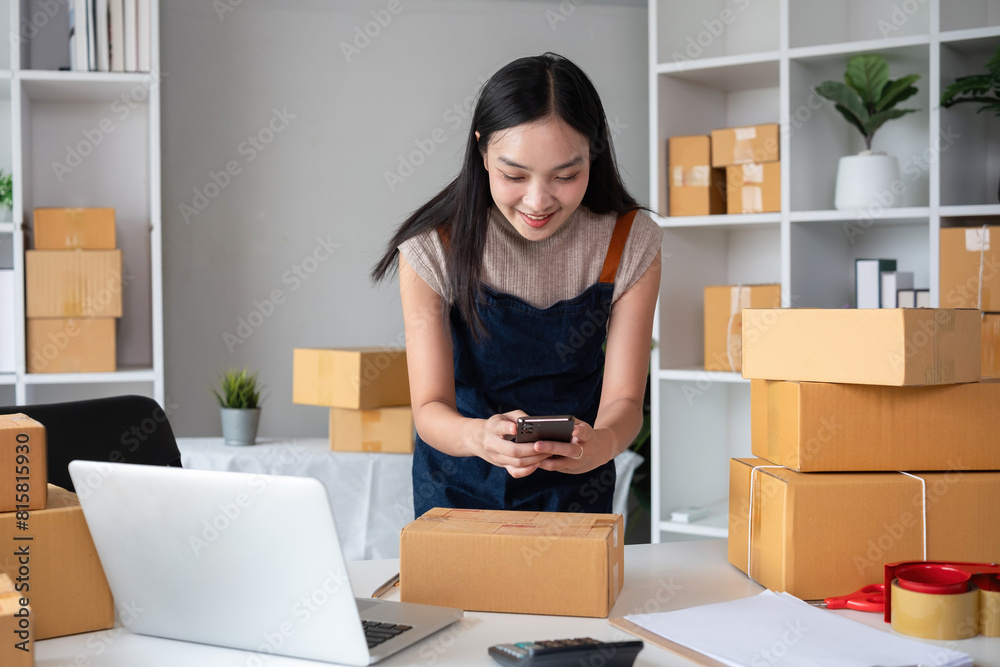 A young woman selling products online takes photos of product boxes after packing them and preparing them for delivery to customers. A young woman selling products online takes photos of product boxes after packing them and preparing them for delivery to customers.