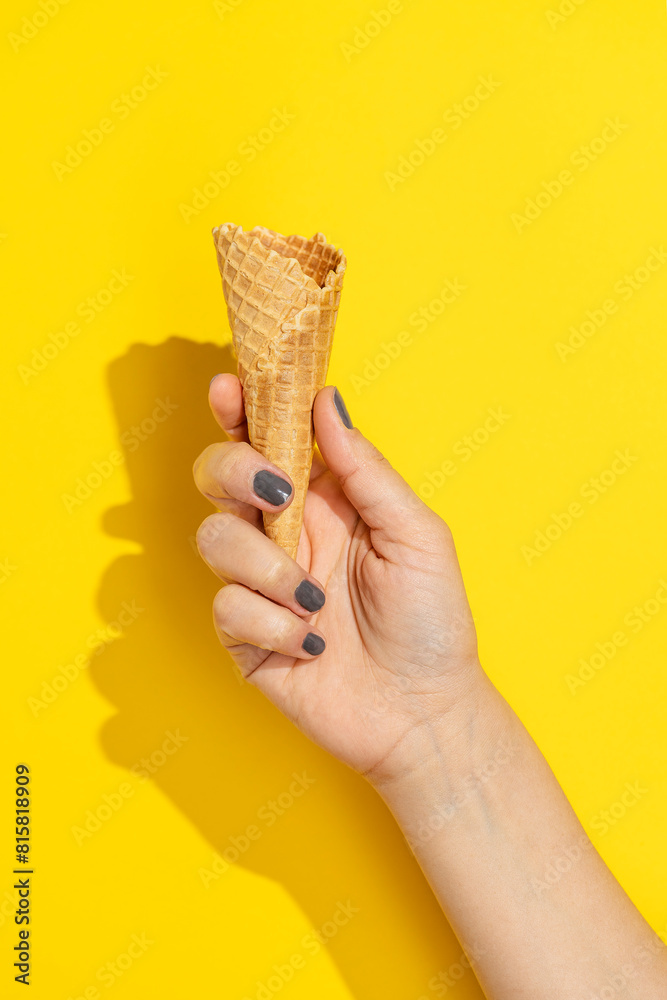 Hand holding empty icecream cone on yellow background Hand holding empty icecream cone on yellow background