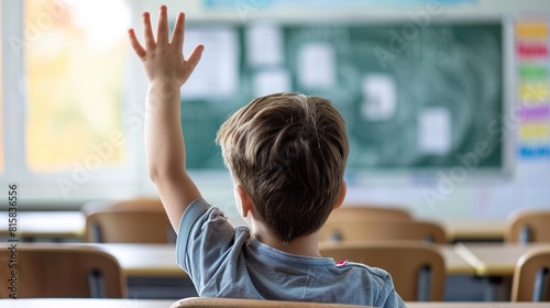 A smart schoolboy sits at a desk in a classroom with his hand raised, wanting to give the correct answer or participate. Concept of education, primary school, learning photo