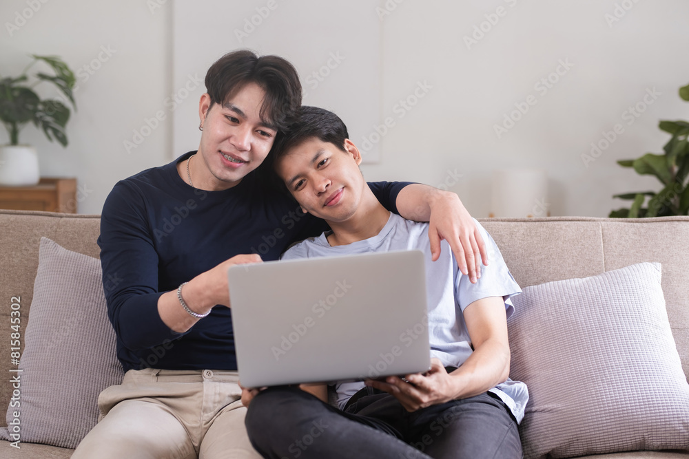 A gay couple spends their free time sitting on a laptop doing activities together on a holiday in the living room. A gay couple spends their free time sitting on a laptop doing activities together on a holiday in the living room.