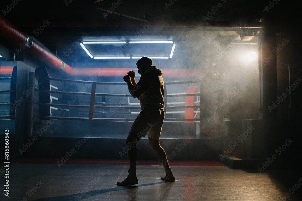 A male boxer is boxing with a shadow on the background of a boxing ring. A boxer practices his punches in a boxing studio.