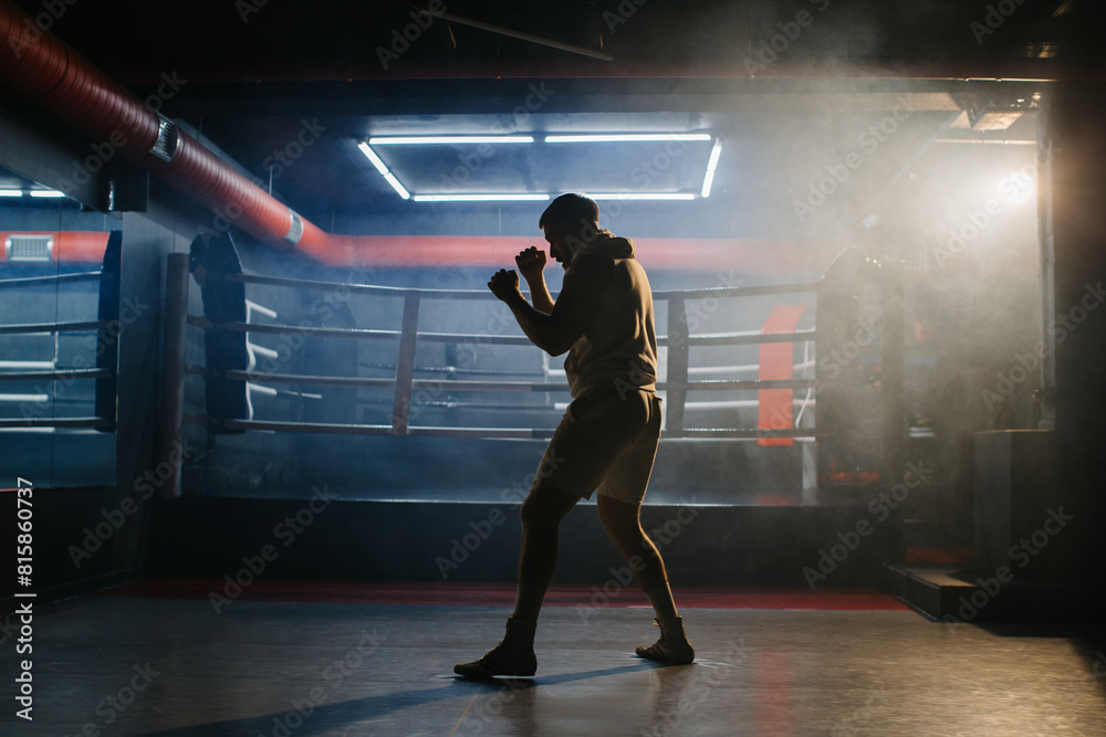 A male boxer is boxing with a shadow on the background of a boxing ring. A boxer practices his punches in a boxing studio. A male boxer is boxing with a shadow on the background of a boxing ring. A boxer practices his punches in a boxing studio.