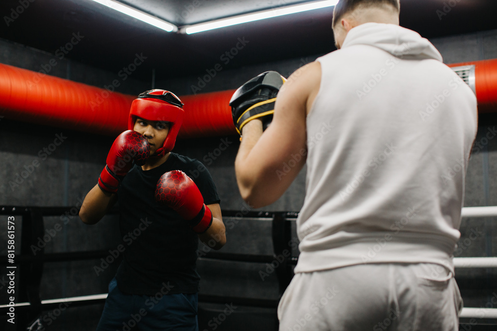 A teenager wearing a red protective helmet and gloves trains in a boxing ring with a coach. A teenager wearing a red protective helmet and gloves trains in a boxing ring with a coach.