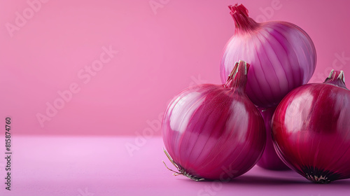 A beautiful close-up photograph of a trio of red onions against a pink background. The onions are perfectly round and smooth, with a deep, rich color.