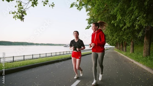 wo pretty women communicate with each other while doing sports. Two young girls in red clothes running in the park. Spend time with friends. TMorning or evening jogging along the river embankment. photo