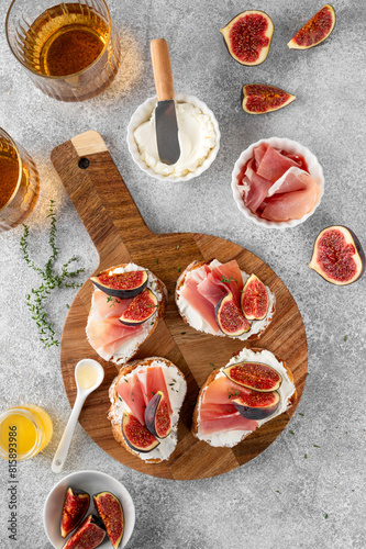 Bruschetta or toast with goat cheese spread, prosciutto, figs and honey on a board.