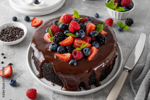 Delicious chocolate cake with chocolate glaze and fresh berries on a white plate on a gray concrete background.